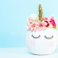 Craft pumpkin painted white and decorated with pink flowers as unicorn on blue background.