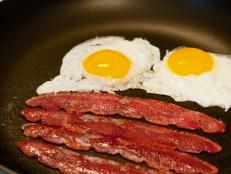 Fried eggs and bacon cooking in a skillet