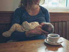 A young mother is breastfeeding her baby in a cafe while she is having a coffee