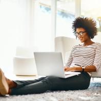 Shot of a cheerful young woman doing online shopping on her laptop while being seated on the floor at home