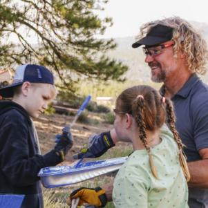 Kody smiles with kids Solomon and Ariella as they paint picnic tables on Coyote Pass.